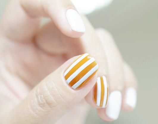 第二步：借助贴纸在大拇指和中指上画出白色条状，让指甲呈现黄白相间的纹理。照干